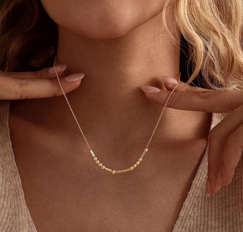 Gold Morse code necklace worn with hands framing the chain
