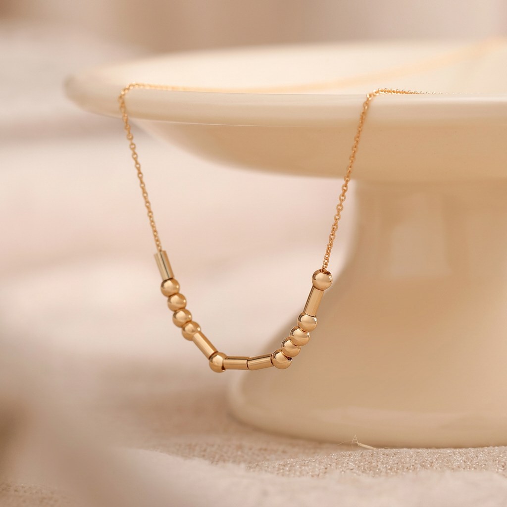 Gold Morse code necklace draped on an ivory dish